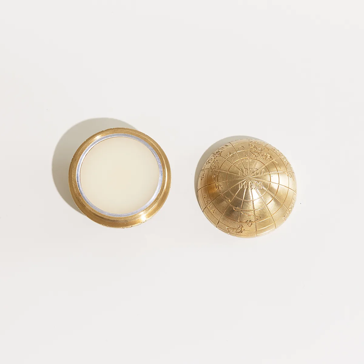 The brass globe open, showing the solid parfum